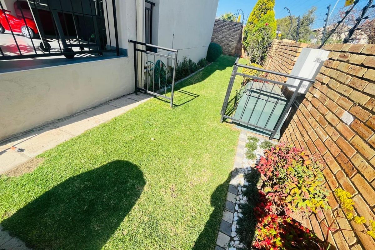 A side garden area featuring a manicured lawn, brick boundary wall with electric fencing, and a metal security gate.