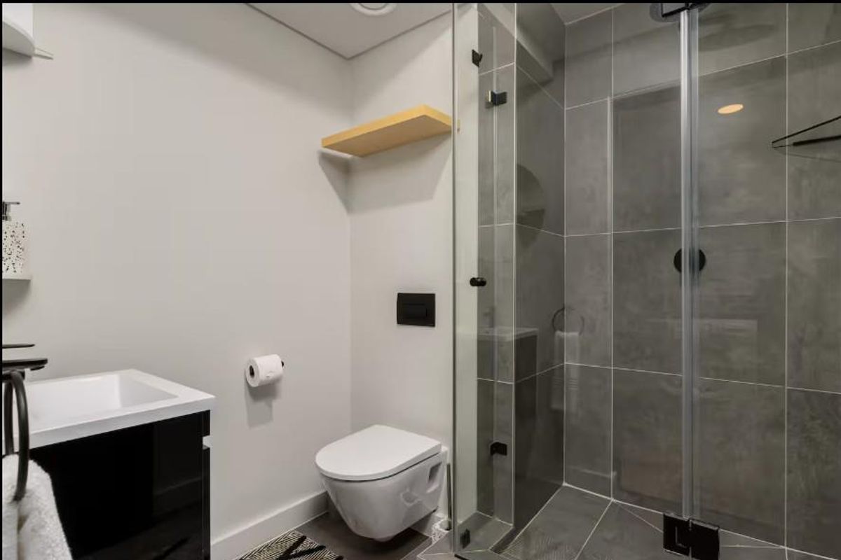 Modern bathroom featuring a wall-mounted toilet, glass-enclosed walk-in shower with grey tiling, and a sleek vanity unit.