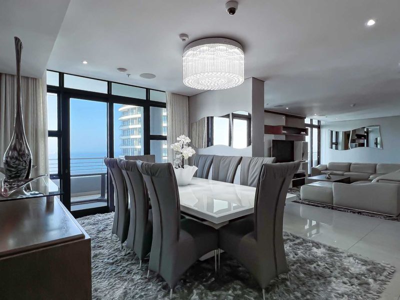 Spacious open-plan living and dining area featuring large floor-to-ceiling windows with ocean views, recessed lighting, and modern tiled flooring.