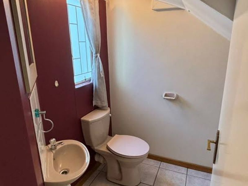 A compact guest bathroom featuring a wall-mounted basin, toilet, and tiled flooring, situated under a sloped ceiling.