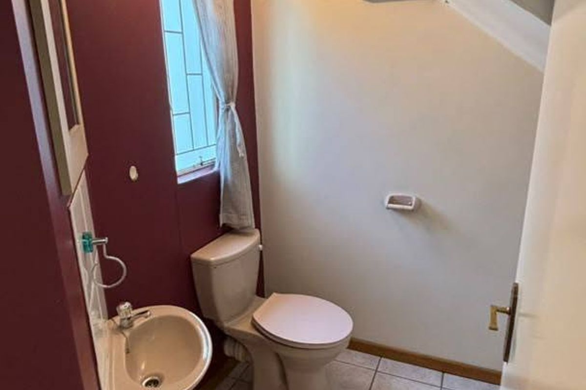 A compact guest bathroom featuring a wall-mounted basin, toilet, and tiled flooring, situated under a sloped ceiling.