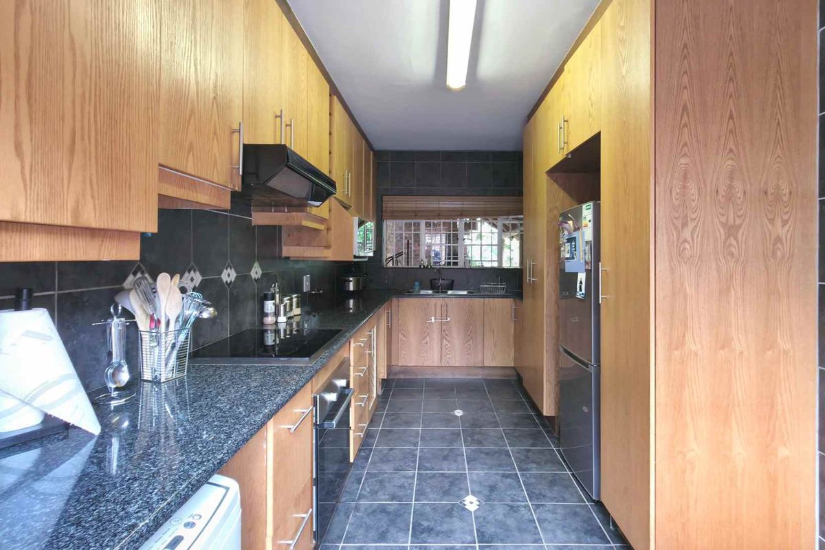 Galley-style kitchen featuring wood-veneer cabinetry, dark granite countertops, tiled backsplash, and integrated oven with extractor fan.