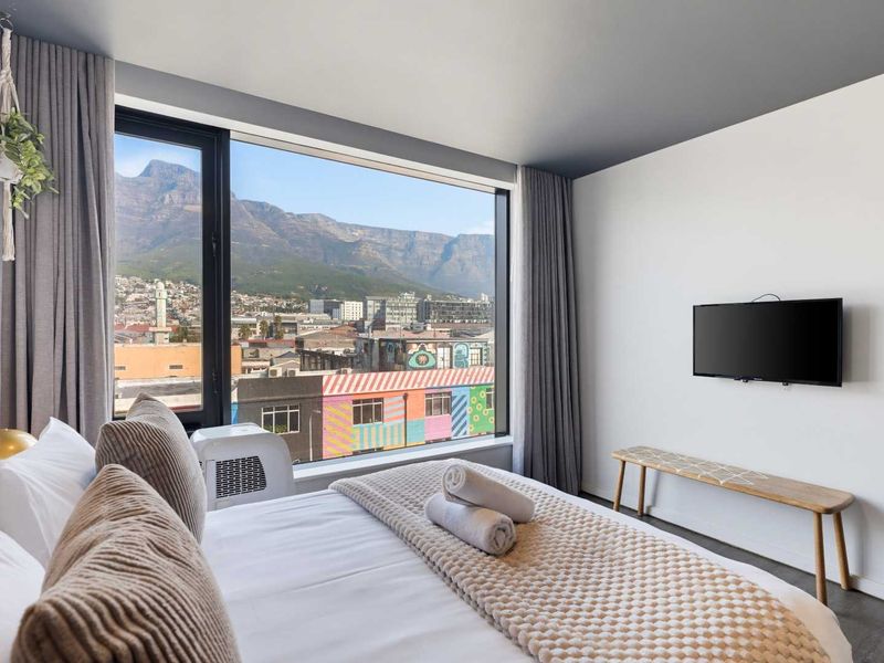 Modern bedroom featuring a large picture window with expansive mountain and city views, complemented by clean finishes and a wall-mounted television.