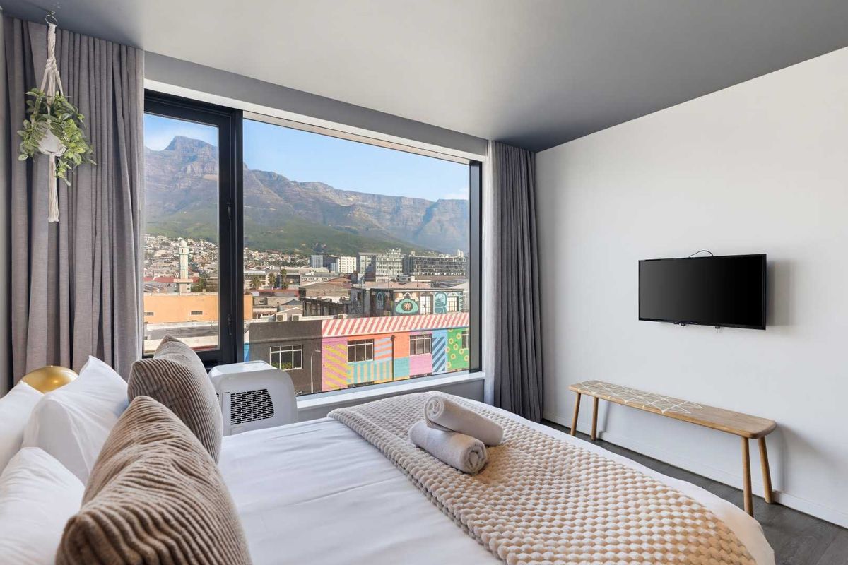 Modern bedroom featuring a large picture window with expansive mountain and city views, complemented by clean finishes and a wall-mounted television.