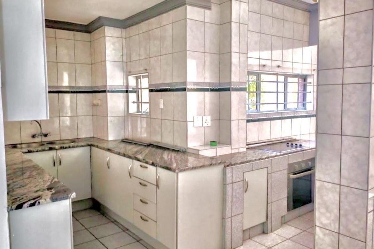 A functional kitchen featuring granite countertops, built-in oven, hob, and tiled finishes throughout, offering a clean and practical workspace.