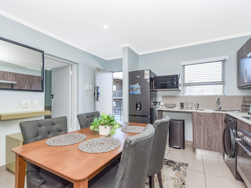 An open-plan kitchen and dining area featuring modern wood-finish cabinetry, integrated appliances, tiled flooring, and neutral wall tones.