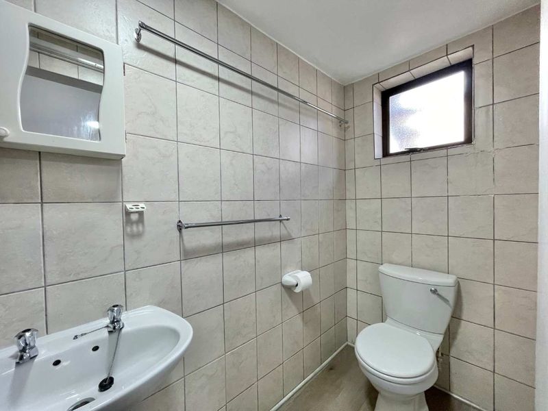 A functional bathroom featuring full-height ceramic wall tiling, a pedestal basin with chrome fixtures, and a standard toilet.