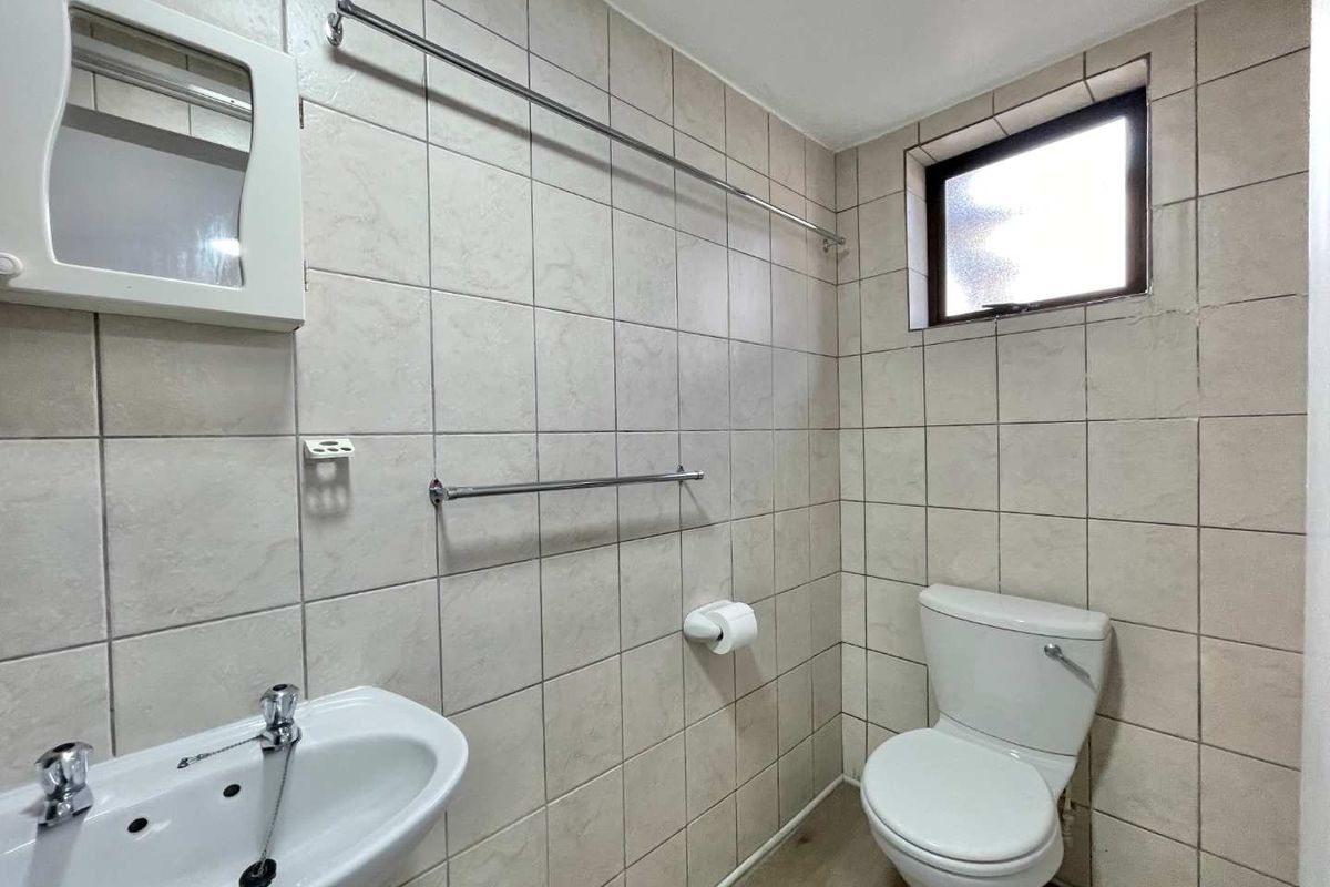 A functional bathroom featuring full-height ceramic wall tiling, a pedestal basin with chrome fixtures, and a standard toilet.