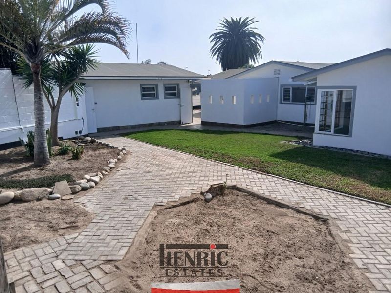 Rear exterior view of the property featuring a paved walkway, established lawn, and white-painted building facades with aluminium window frames.