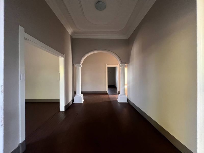 Spacious hallway featuring an elegant arched entryway with decorative columns, ornate ceiling molding, and dark hardwood flooring.