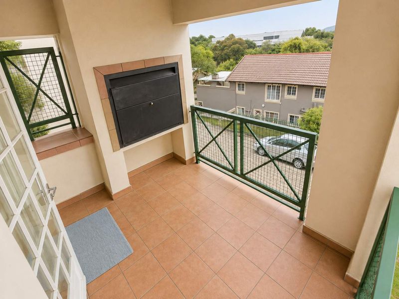 A covered balcony featuring tiled flooring, a built-in braai, and a metal balustrade, offering an outdoor space for relaxation.