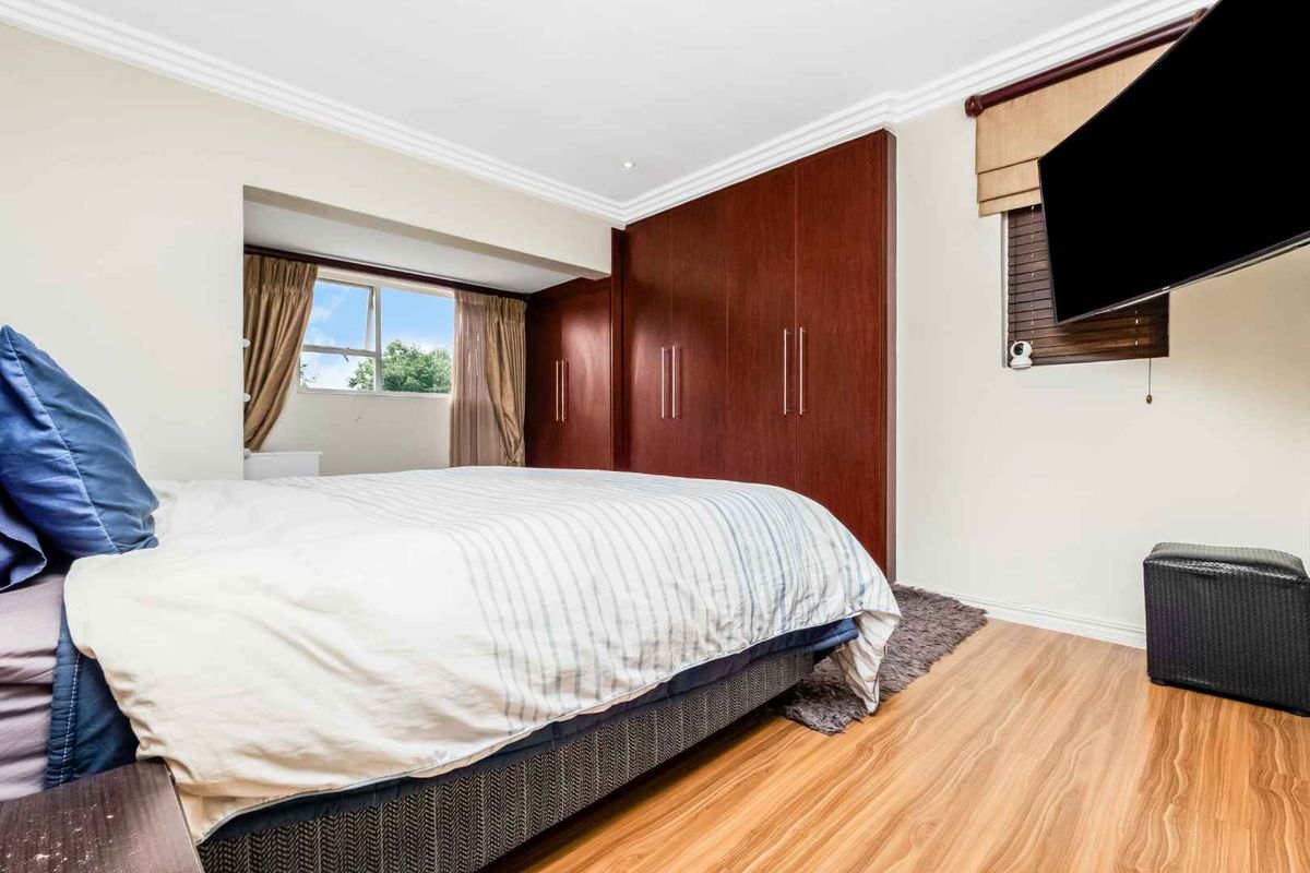 A well-maintained bedroom featuring built-in wooden cabinetry, laminate flooring, and crown molding, offering a clean and functional living space.