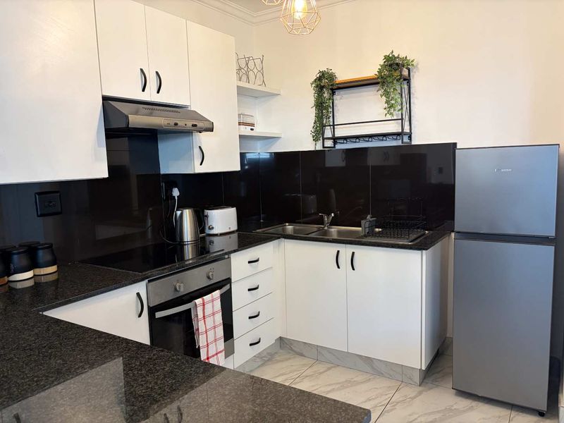 Modern kitchen featuring white cabinetry, black granite countertops, a sleek black glass splashback, and integrated stainless steel appliances.