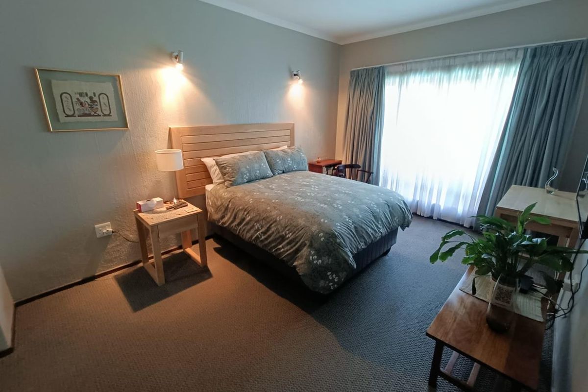 A comfortable bedroom featuring wall-mounted accent lighting, a built-in headboard, and large windows with curtains allowing for natural light.