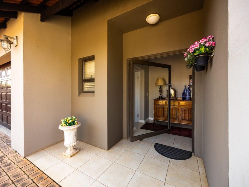 A welcoming covered entrance area featuring tiled flooring, a modern pivot door, and integrated exterior lighting, providing access to the home.