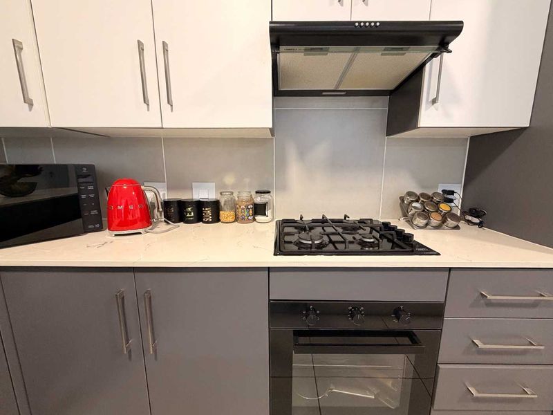 Modern kitchen featuring grey lower cabinets, white upper cabinetry, quartz countertops, a gas hob, built-in oven, and a sleek extractor fan.