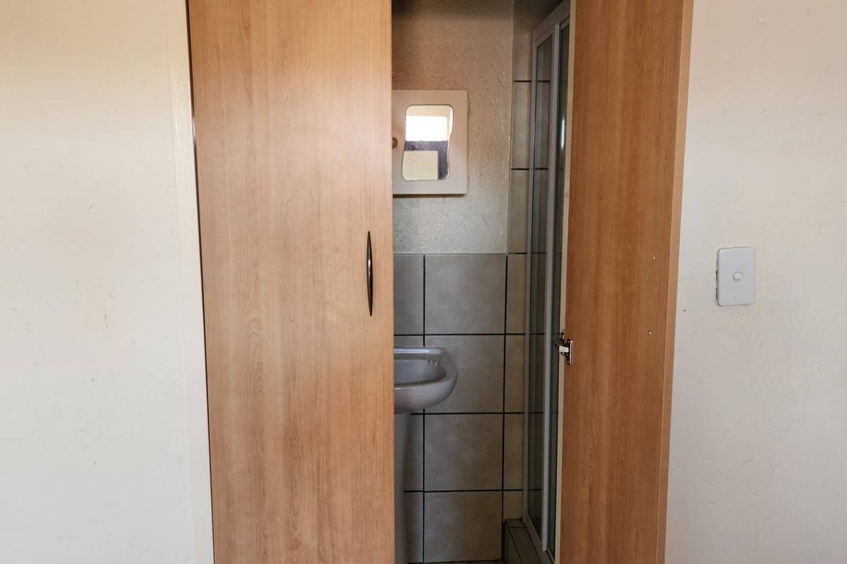 A compact bathroom featuring a pedestal basin and shower enclosure, accessed through a wooden door.