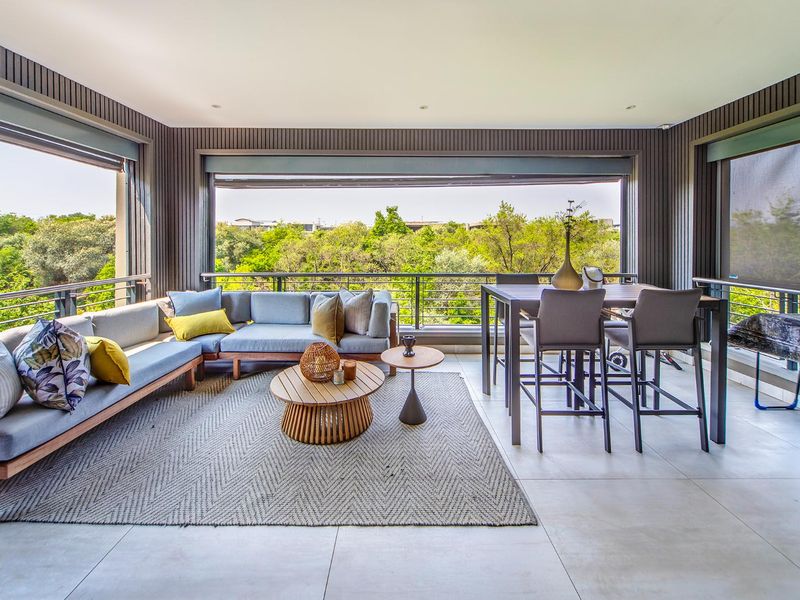Spacious covered balcony featuring modern tiled flooring, vertical slat wall detailing, and a metal balustrade, offering an open-air feel with scenic green views.