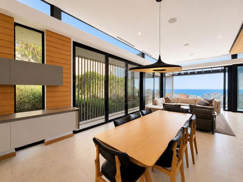 Modern open-plan living and dining area featuring floor-to-ceiling glass doors, timber wall accents, and expansive ocean views.