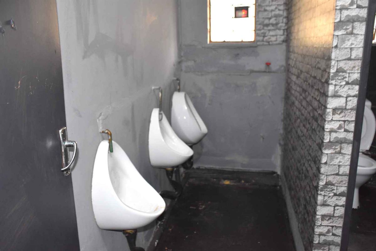 A utilitarian bathroom facility featuring multiple wall-mounted urinals and a toilet, requiring significant maintenance and cosmetic updates to improve its current condition.