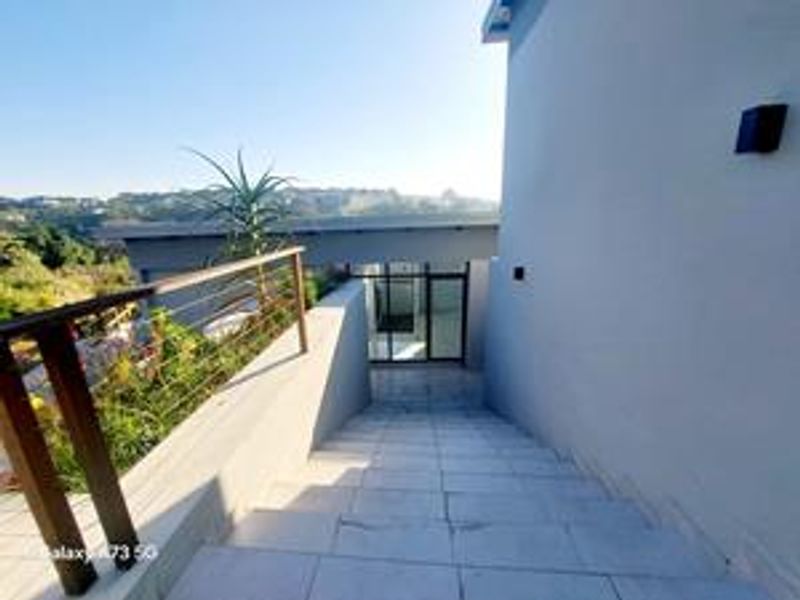 An exterior view of a modern tiled staircase leading down to a glass entrance door, featuring a metal balustrade and scenic hillside views.