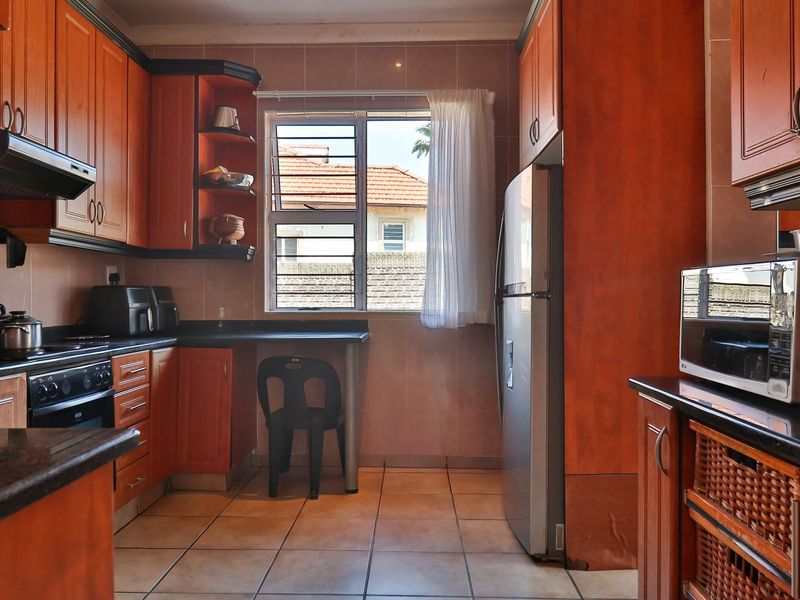 A functional kitchen featuring wooden cabinetry, granite countertops, built-in oven, extractor fan, and tiled flooring with a window providing natural light.