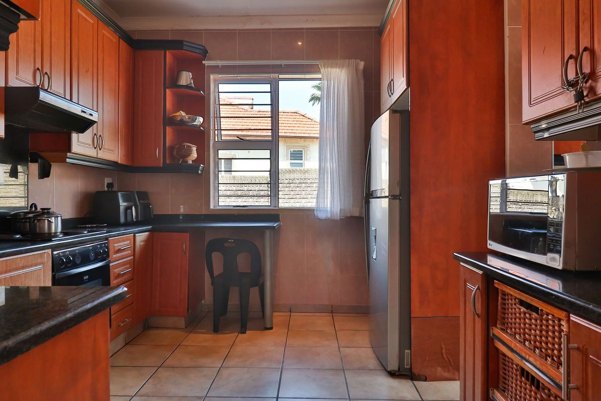 A functional kitchen featuring wooden cabinetry, granite countertops, built-in oven, extractor fan, and tiled flooring with a window providing natural light.