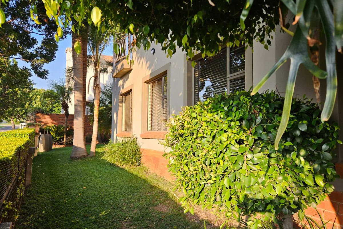 A view of the side exterior of the house featuring a well-maintained lawn, mature trees, and established garden shrubs.