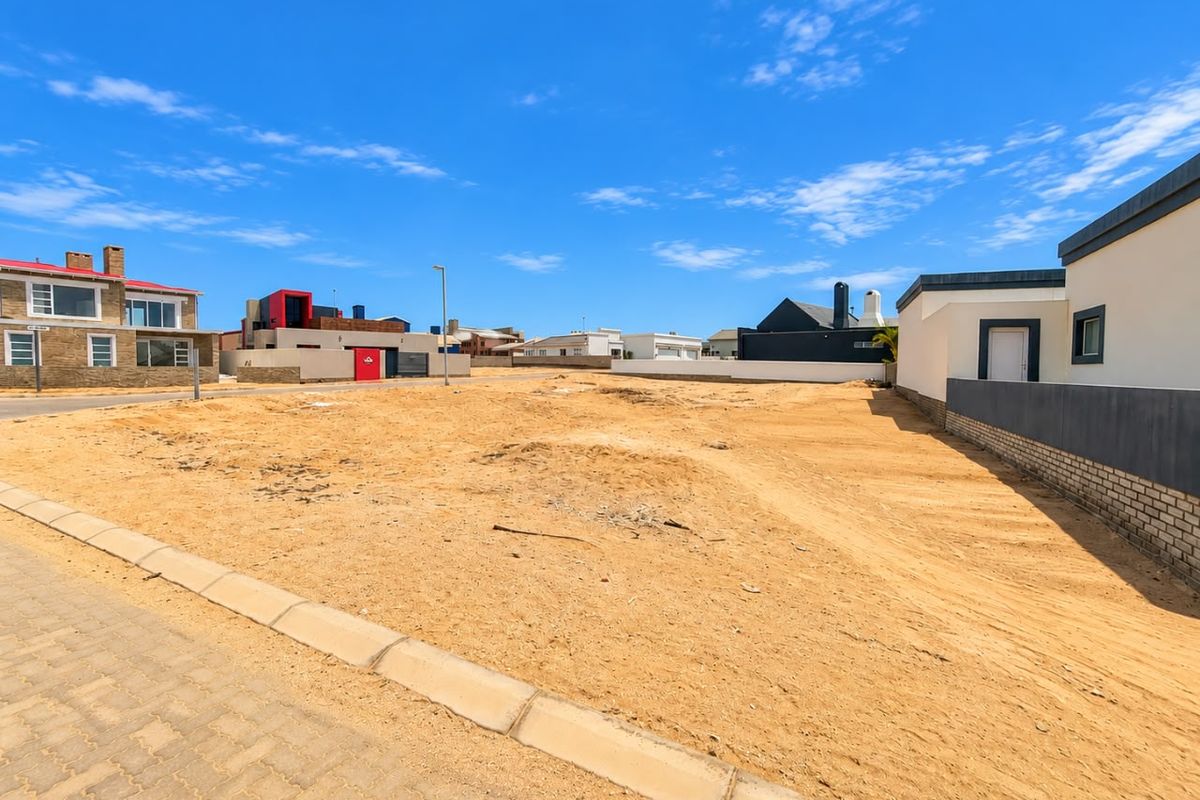 A vacant residential plot featuring a level sandy surface, paved curb, and established boundary walls in a developed neighborhood.