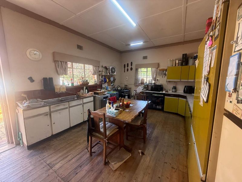 Spacious kitchen featuring timber flooring, built-in cabinetry, and a double sink, offering a functional layout with potential for modern updates.