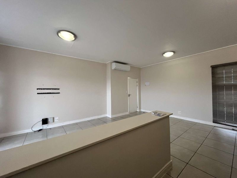 An open-plan living area featuring neutral tiled flooring, a wall-mounted air conditioning unit, and clean, well-maintained finishes throughout the space.