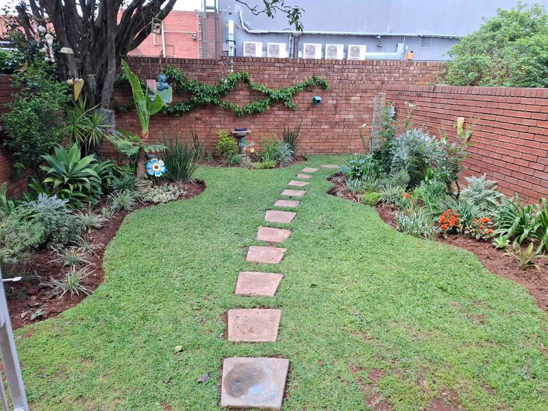 A well-maintained private garden featuring a stone paver path, established garden beds, and a secure brick boundary wall.