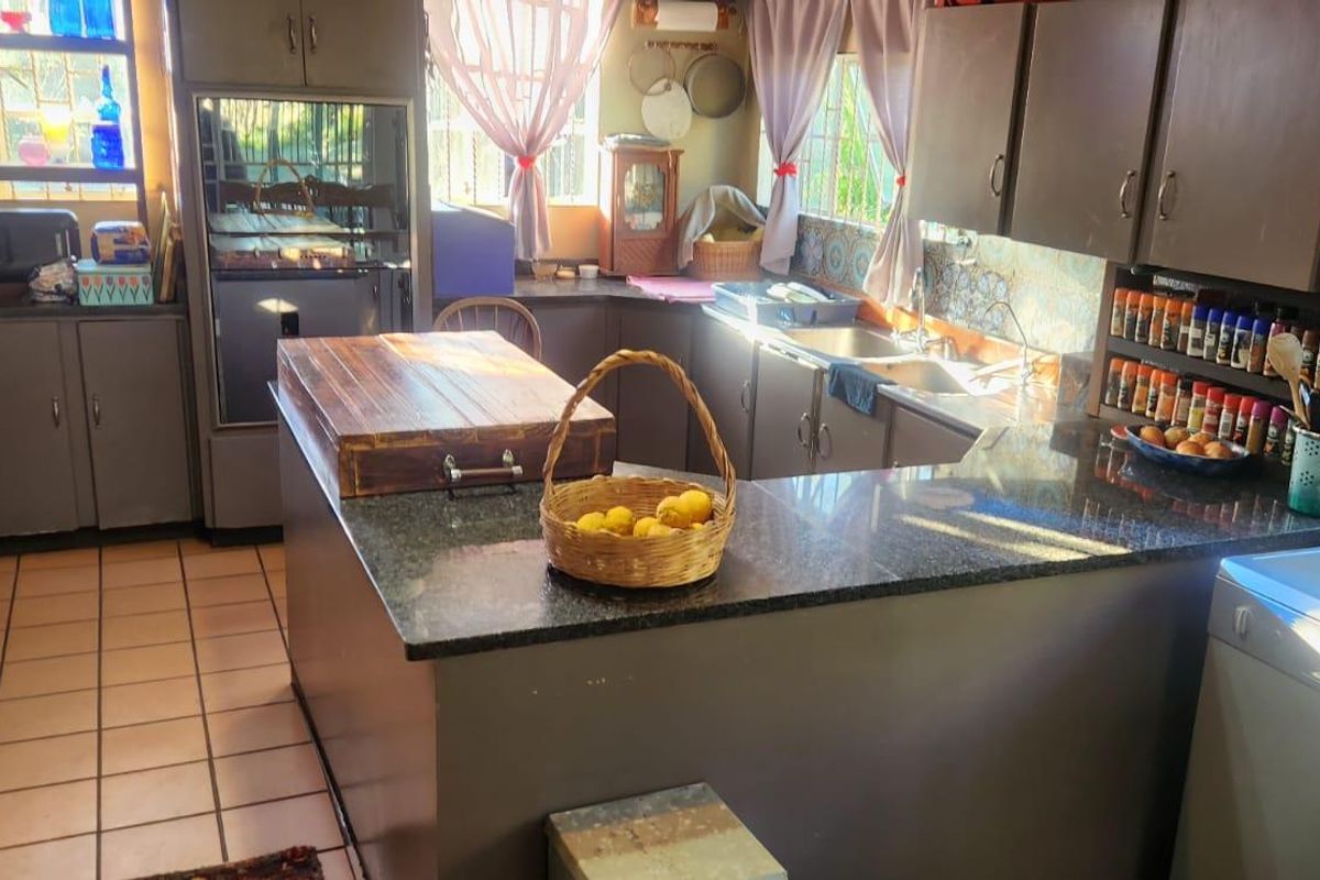 A functional kitchen featuring dark cabinetry, granite countertops, a double basin sink, and tiled flooring with natural light from multiple windows.