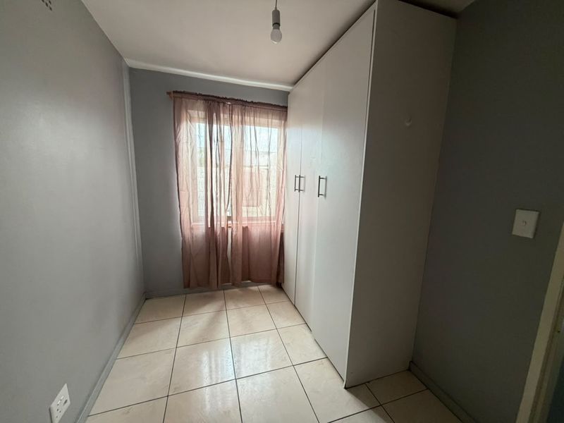 A compact bedroom featuring neutral grey walls, tiled flooring, and a large built-in wardrobe, offering a clean and functional space.