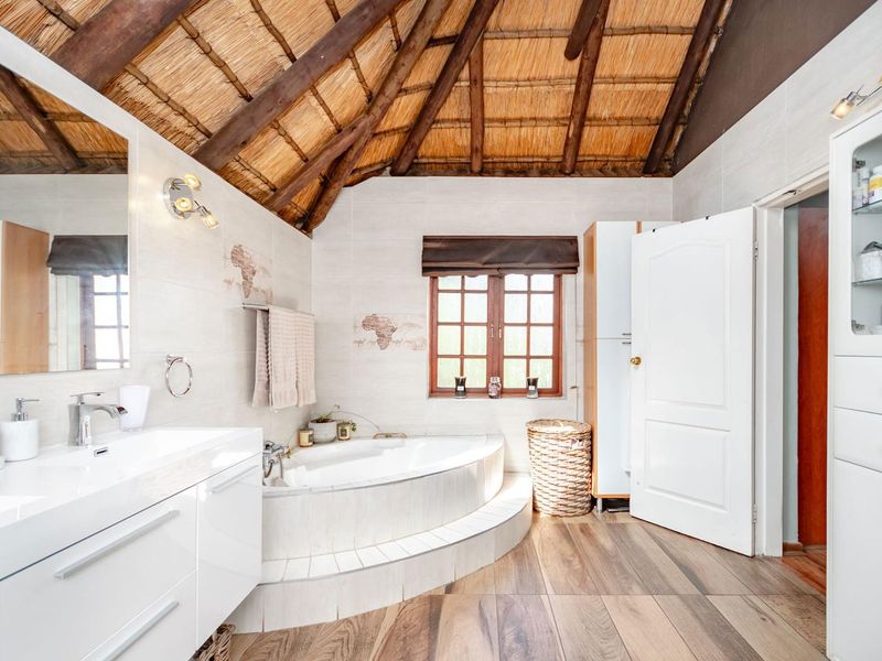 A well-maintained bathroom featuring a corner bathtub, modern vanity, and unique vaulted thatched ceiling with exposed timber beams.