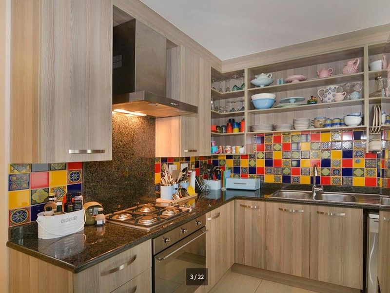 A functional kitchen featuring granite countertops, a gas hob, built-in oven, stainless steel extractor fan, and vibrant multi-colored tiled splashbacks with ample cabinetry.