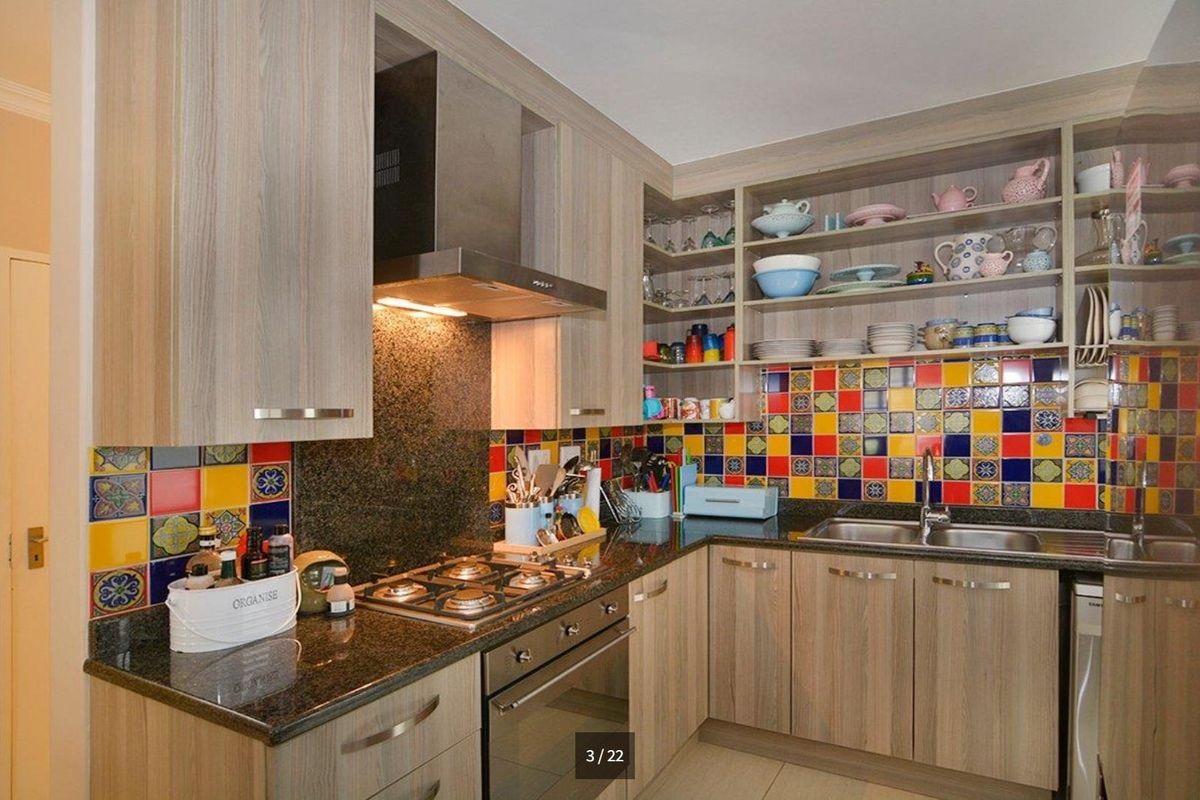 A functional kitchen featuring granite countertops, a gas hob, built-in oven, stainless steel extractor fan, and vibrant multi-colored tiled splashbacks with ample cabinetry.