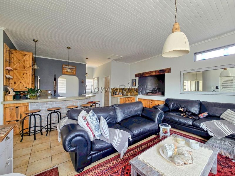 Spacious open-plan living area featuring a brick breakfast bar, built-in indoor braai, timber cabinetry, and a distinctive tongue and groove ceiling.