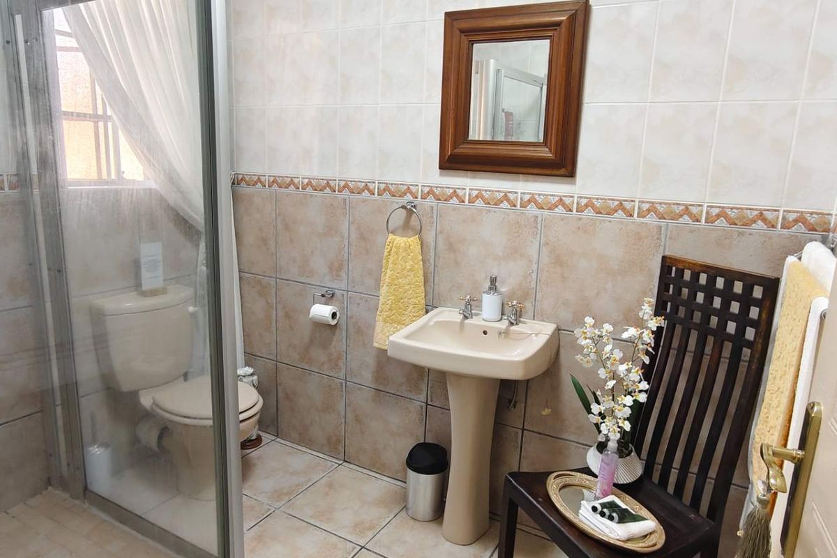A functional bathroom featuring a pedestal basin, a glass-enclosed shower, and a toilet, finished with neutral ceramic wall and floor tiling.