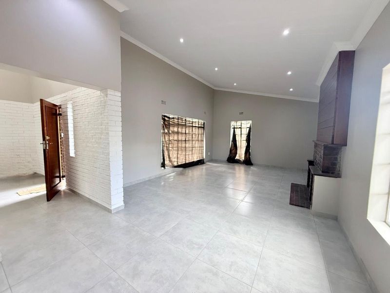 Spacious, light-filled living area featuring neutral tiled flooring, recessed downlights, and a prominent brick fireplace, offering a clean and versatile blank canvas.