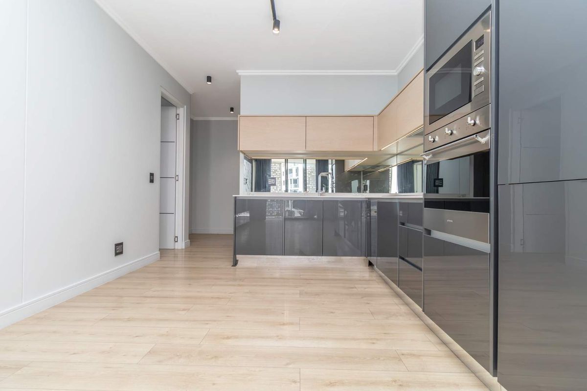 Modern kitchen featuring sleek grey and light wood cabinetry, integrated appliances, mirror splashback, and high-quality laminate flooring in an open-plan layout.