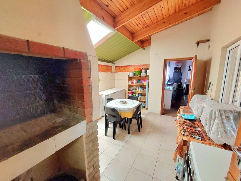 Covered patio area featuring a built-in brick braai, exposed timber beam ceiling, and tiled flooring, offering a functional space for outdoor entertaining.