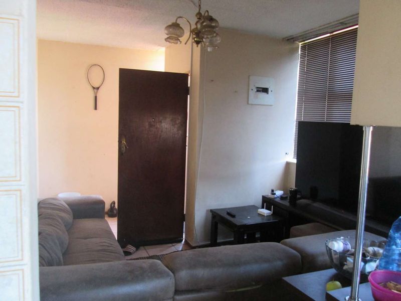 A living room area featuring a window with venetian blinds, a ceiling light fixture, and an electrical distribution board mounted on the wall.