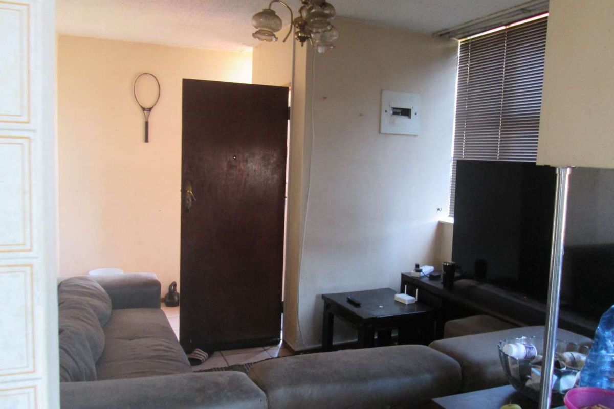 A living room area featuring a window with venetian blinds, a ceiling light fixture, and an electrical distribution board mounted on the wall.