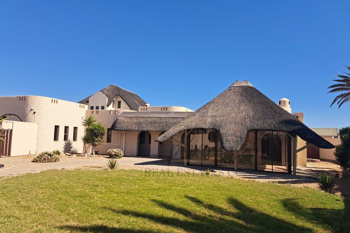 A rear view of the house featuring a distinctive thatched roof, paved patio area, and well-maintained garden space.