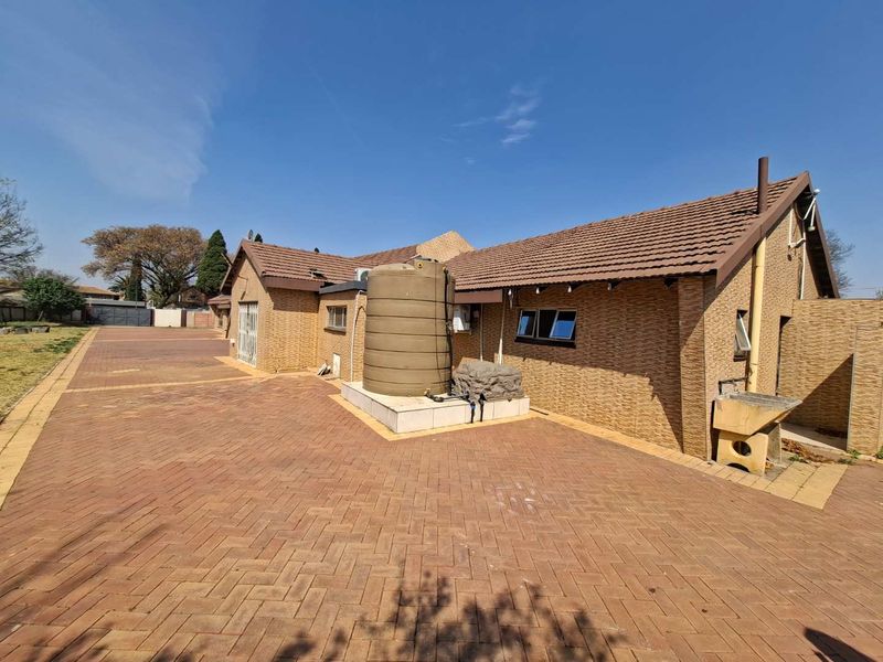 Rear exterior view of the property featuring extensive brick paving, a water storage tank, and a well-maintained facebrick facade with a tiled roof.