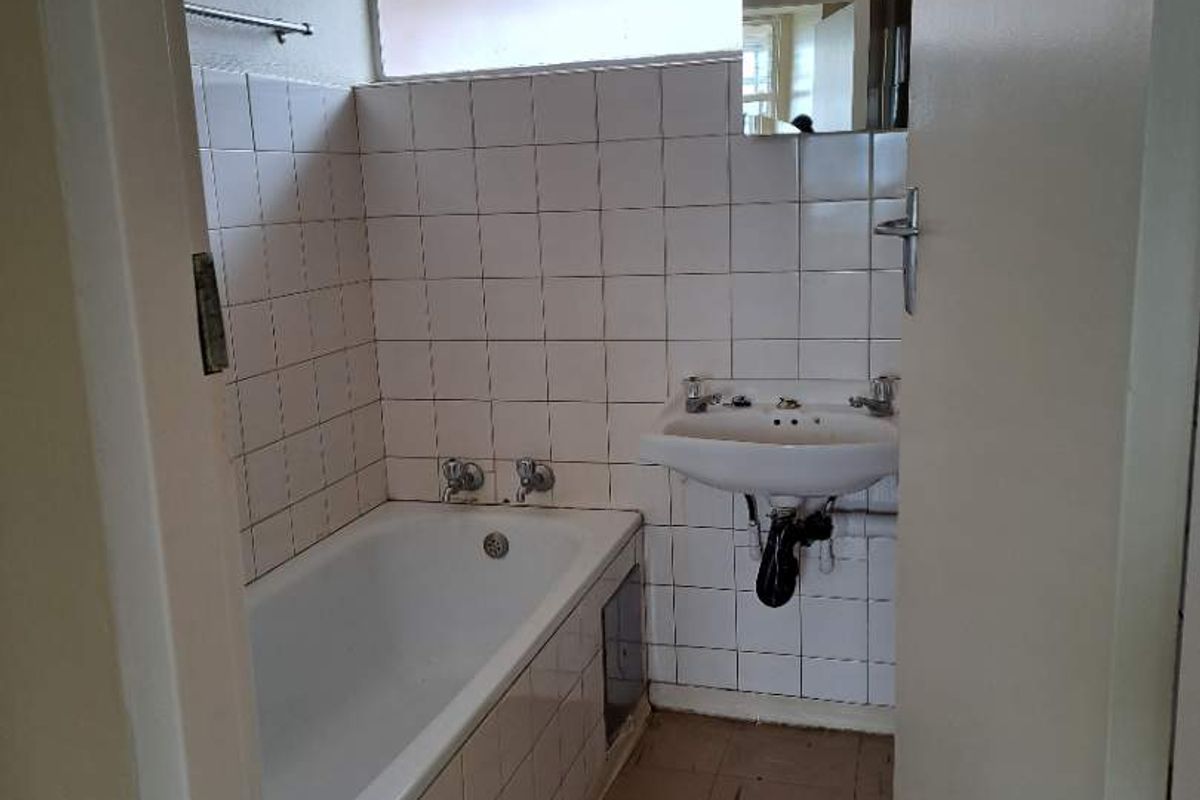 A dated bathroom featuring a standard bathtub, wall-mounted basin, and tiled walls, requiring modernization to improve functionality and aesthetic appeal.