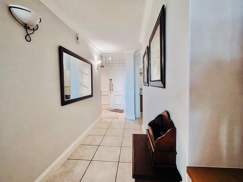 A bright, well-maintained hallway featuring neutral tiled flooring, decorative coving, and wall-mounted lighting fixtures leading to the main entrance.