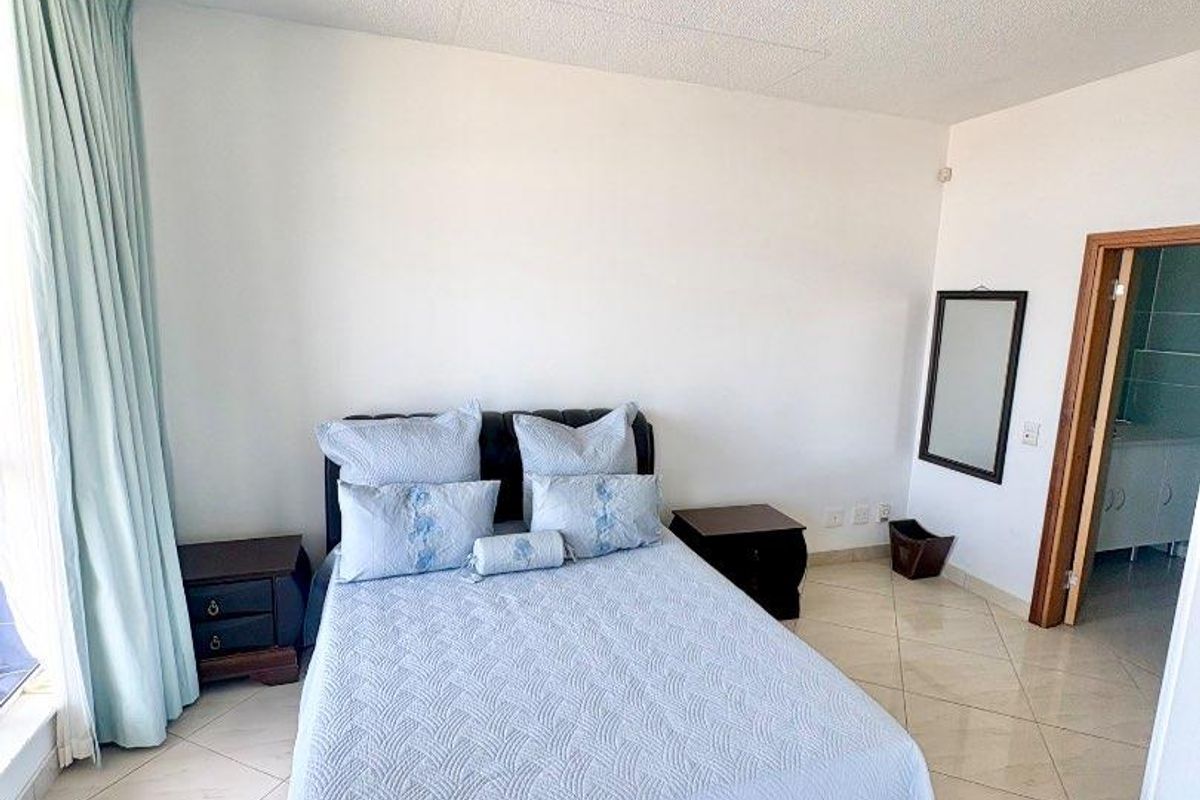 A bedroom featuring tiled flooring, a ceiling-mounted light fixture, and an adjacent doorway leading to an en-suite bathroom.