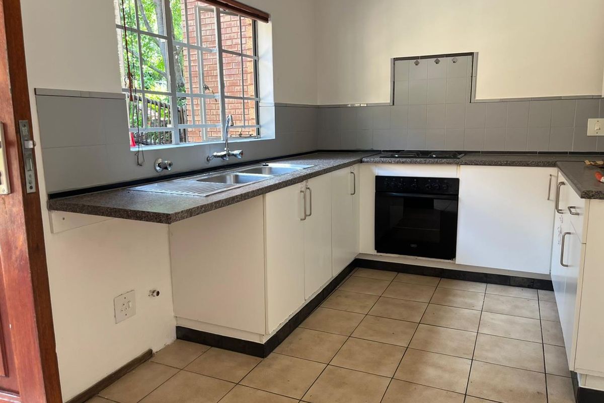 Functional kitchen featuring white cabinetry, granite-look countertops, a built-in oven and hob, and a double stainless steel sink with a window view.